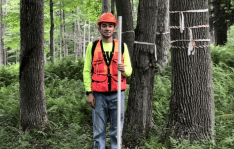 Brandon Marcucci '21站在阿勒格尼国家森林的树木中，用齿轮测量树木.